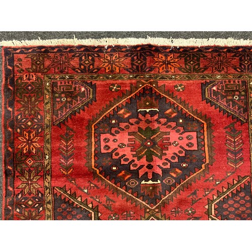 2068 - A Hamadan rug, knotted with a central row of three hexagonal shape medallions, in rich tones of red,... 