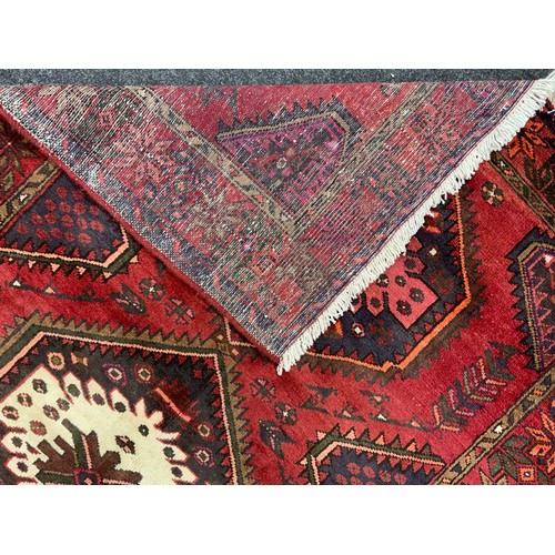 2068 - A Hamadan rug, knotted with a central row of three hexagonal shape medallions, in rich tones of red,... 