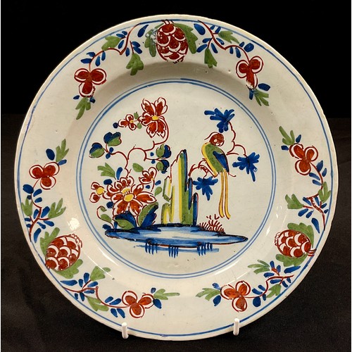 1261 - A Lambeth Delft plate, painted with a central roundel of a parrot on a branch by a cliff with flower... 