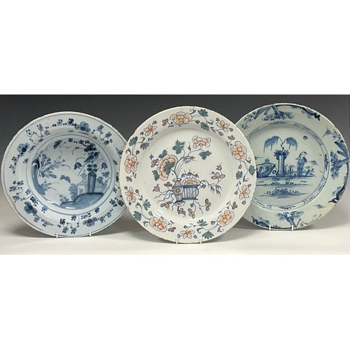 1254A - A 18th century English Delftware plate, decorated with vases on plinth, peonies and twining vines, t... 