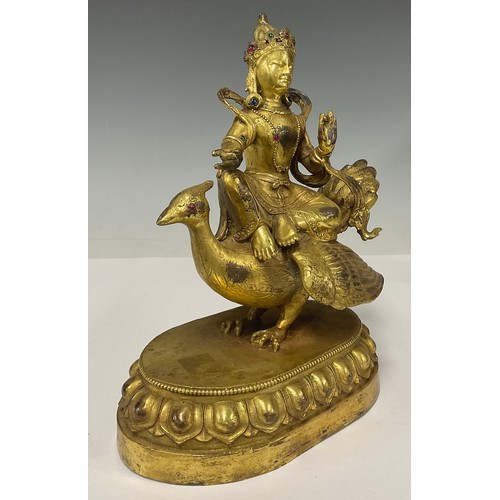 514 - A gilt bronze jewelled figure, as a seated Buddha riding on a peacock, oval lotus base, 17cm wide, 2... 