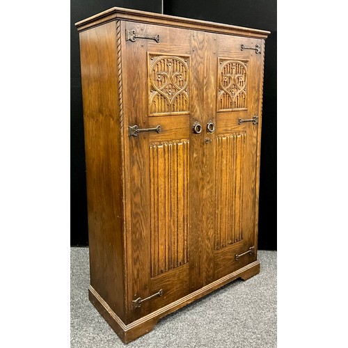 133 - A mid 20th century priory style oak wardrobe and matching tall boy, each with carved linen-fold door... 