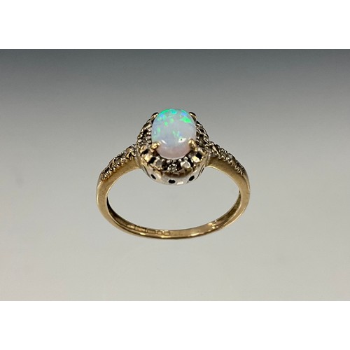 913 - An opal and diamond ring, oval cabochon opal flashing green, blue and orange play, with diamond acce... 