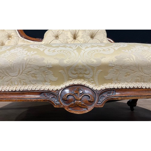 2464 - A Victorian walnut chaise longue, stuffed-over upholstery, the frame carved with bell husks and flow... 