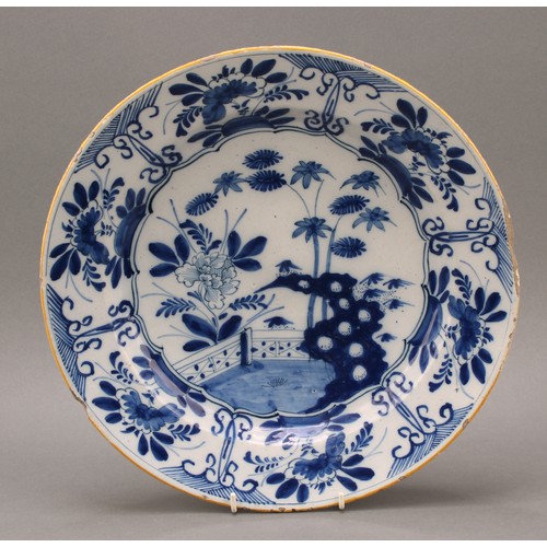 16 - An 18th century Delftware charger, decorated in the Chinese taste in underglaze blue with a fence, f... 