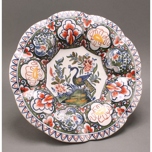 6 - A Delft lobed circular dish, painted in polychrome, with a peacock in a garden setting, the rim with... 