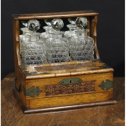 2563 - An Art & Crafts period oak tantalus cabinet, the three cut glass decanters restrained within a mirro... 