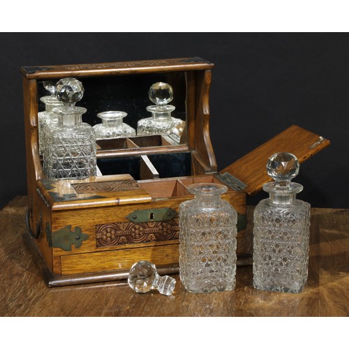 2563 - An Art & Crafts period oak tantalus cabinet, the three cut glass decanters restrained within a mirro... 