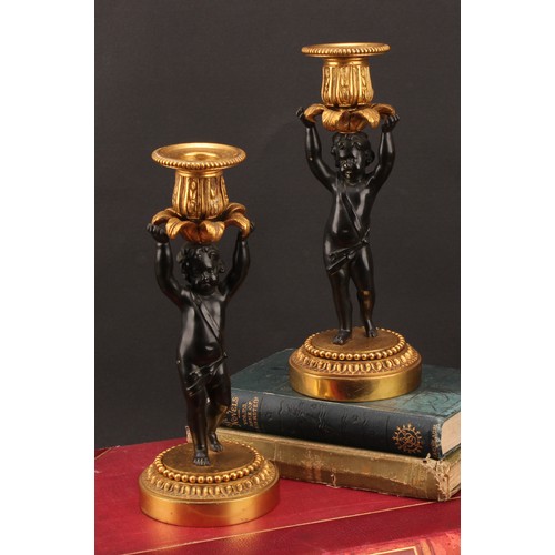 2083 - A pair of French Bronze and ormolu candlesticks, bronze cherub columns arms erect holding a gilt lea... 