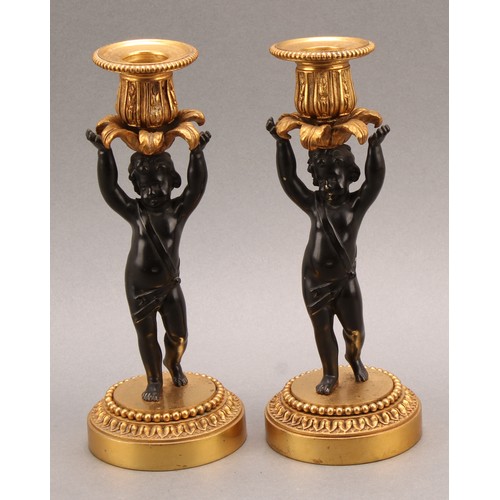 2083 - A pair of French Bronze and ormolu candlesticks, bronze cherub columns arms erect holding a gilt lea... 