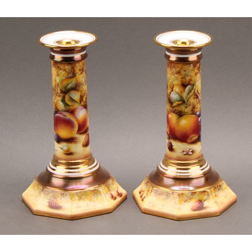 131 - A pair of Royal Worcester candlesticks, painted by Sally Wood, signed, with ripe fruit on a mossy ba... 