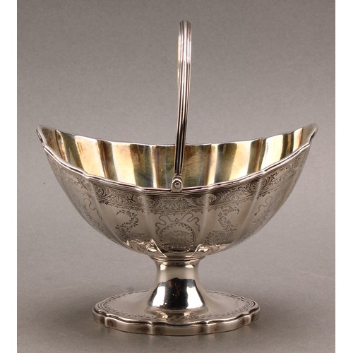 774 - A George III silver fluted boat shaped swing-handled pedestal sugar basket, bright-cut engraved in t... 