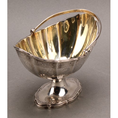 774 - A George III silver fluted boat shaped swing-handled pedestal sugar basket, bright-cut engraved in t... 