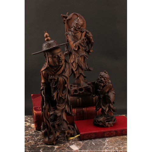 1285 - A 19th century Chinese carved hardwood figure of an elder, standing with peaches, holding beads and ... 