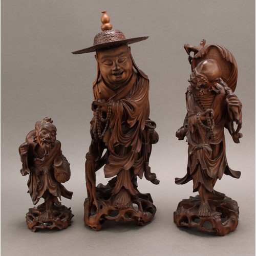 1285 - A 19th century Chinese carved hardwood figure of an elder, standing with peaches, holding beads and ... 