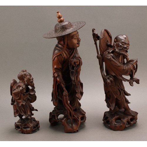 1285 - A 19th century Chinese carved hardwood figure of an elder, standing with peaches, holding beads and ... 