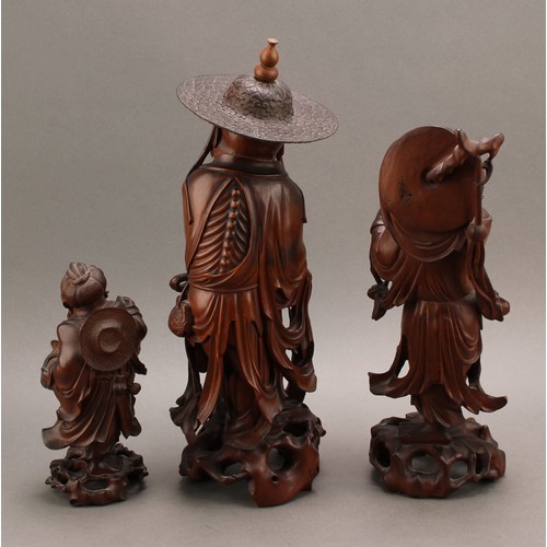 1285 - A 19th century Chinese carved hardwood figure of an elder, standing with peaches, holding beads and ... 