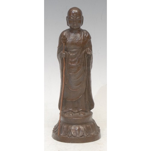 3567 - An early 20th century Tibetan bronze, of a Buddhist monk holding a staff, lotus leaf base, 18cm high... 