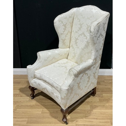 16 - A George II Revival wingback armchair, traditionally upholstered in an ivory coloured damask, concav... 