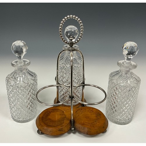 47 - An Edwardian oak and silver plated three bottle stand, with glass decanters, beaded looping handle, ... 