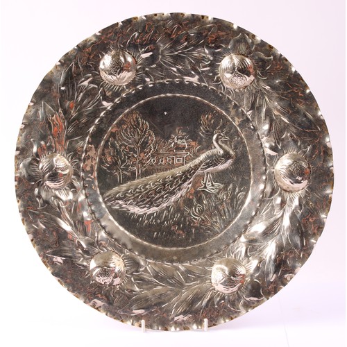 41 - An Arts and Crafts silver plated shaped circular charger, chased with a peacock, the wavy border cha... 