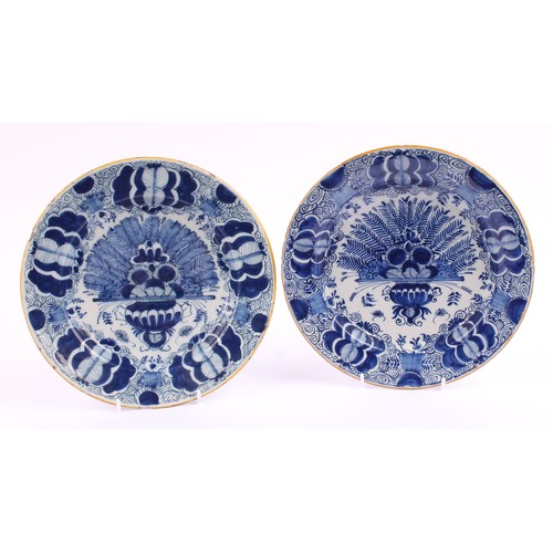 780 - A pair of 18th century Dutch Delft circular plates, painted in tones of blue with vases of flowers a... 