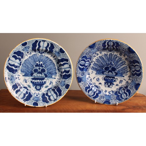 780 - A pair of 18th century Dutch Delft circular plates, painted in tones of blue with vases of flowers a... 