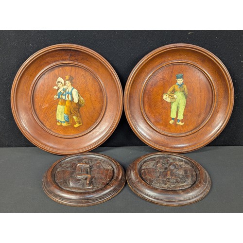 40 - A pair of Black Forest carved plaques, signed; a pair of German wall plaques decorated with traditio... 