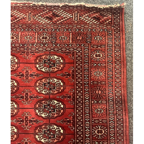A hand knotted Bokhara rug, deep red field with repeating Gül motif to ...
