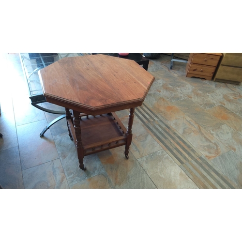 304 - Octagonal wooden side table with lower shelf, featuring turned legs on castor wheels. Crafted from o... 