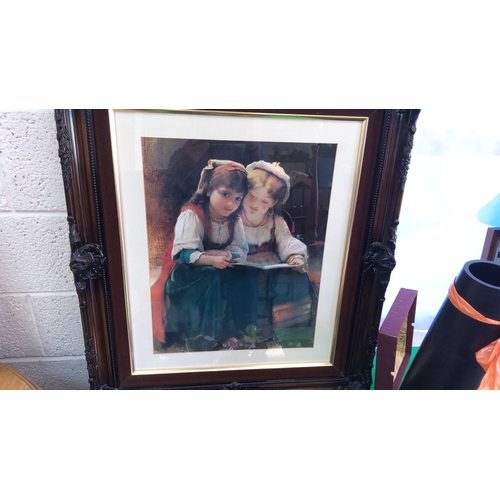 333 - Framed print of two young girls reading. Housed in a dark ornate wooden frame with intricate detaili... 