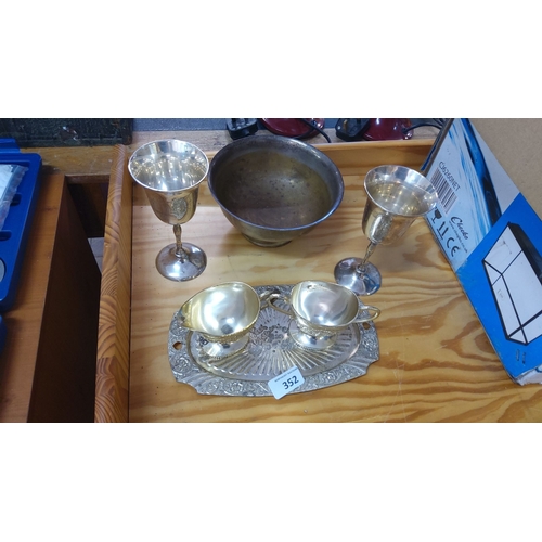 352 - Set of silver-plated items including two goblets, two creamers on an ornate tray, and a brass bowl.