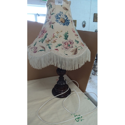 162 - Vintage table lamp with a floral-patterned fabric shade and fringe trim, set on a dark wooden base.