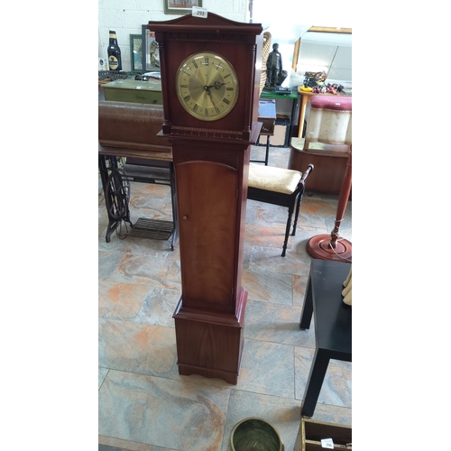 293 - Vintage tallcase clock. Polished wood casing with a brass dial, intricate hands, and Roman numerals.... 