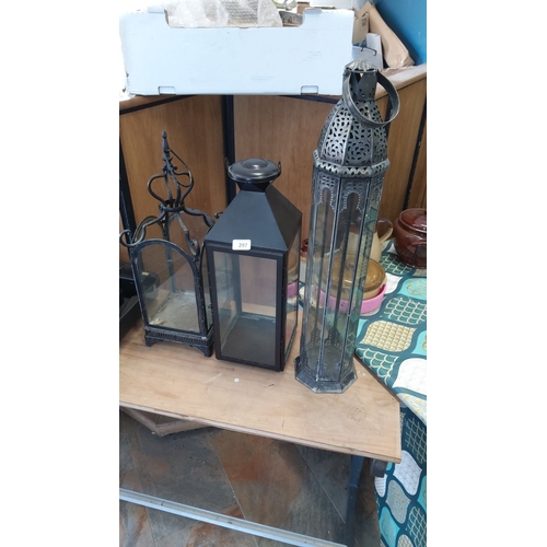 297 - Set of three metal lanterns featuring various intricate designs, glass panes, and pierced detailing.... 