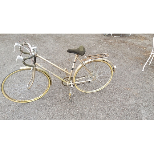 436 - Vintage Raleigh road bicycle with a gold frame, drop handlebars, and rear rack. Iconic design from a... 