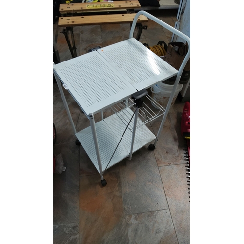 460 - White metal rolling utility cart with two perforated shelves, a wire rack, and a handle. The cart fe... 