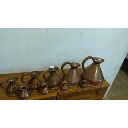 81 - Collection of nine graduating vintage copper jugs, varying sizes, with a classic, bulbous form and g... 