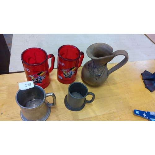 178 - Mixed lot featuring two red glass mugs with cartoon graphics, two metal tankards, and one handcrafte... 