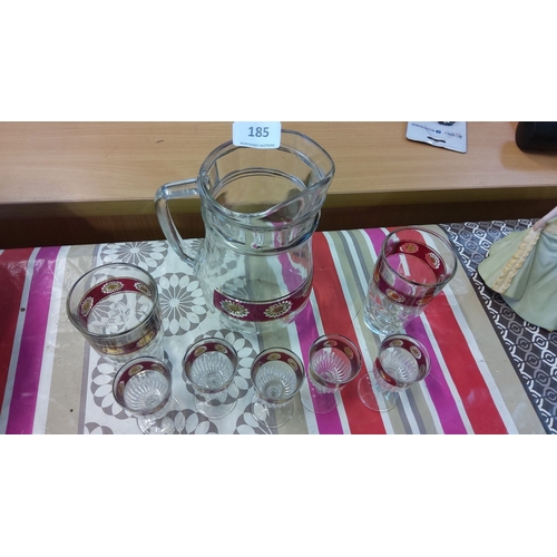 185 - Glass pitcher set with six matching glasses, featuring red and gold floral decorations.