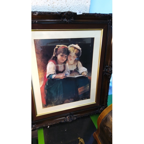 291 - Framed print depicting two young girls reading, surrounded by an ornate dark wood frame with gold in... 