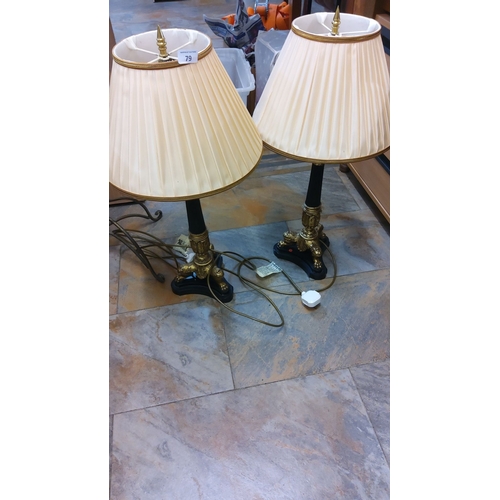 79 - Pair of ornate table lamps with pleated cream shades, featuring gold-colored detailed bases with bla... 