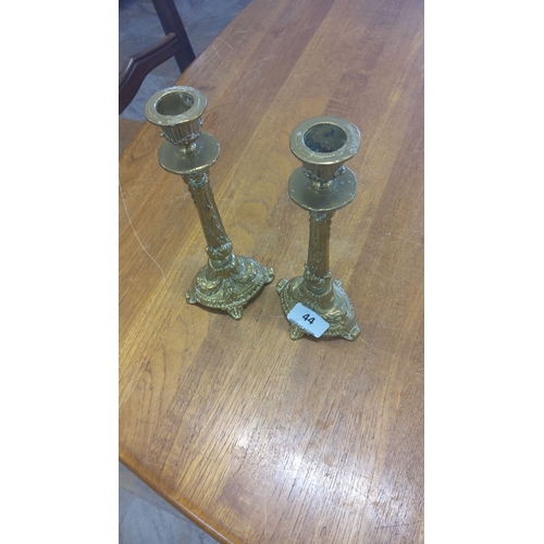 44 - Pair of ornate brass candlesticks with intricate detailing, featuring a classic decorative motif and... 