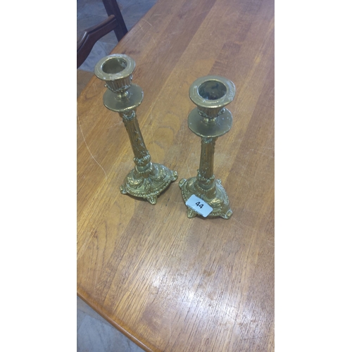 44 - Pair of ornate brass candlesticks with intricate detailing, featuring a classic decorative motif and... 