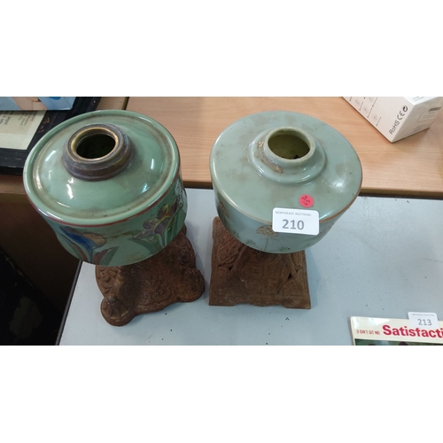 210 - Pair of vintage ceramic oil lamp bases featuring floral motifs, atop ornate carved wooden bases.