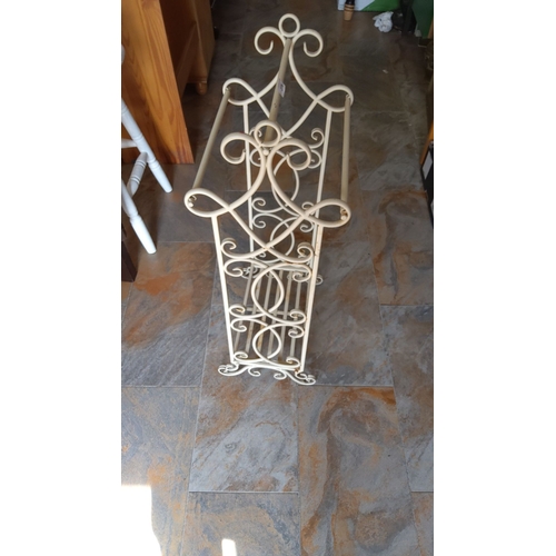 276 - Cream wrought iron magazine rack with decorative scrollwork design. 20th century.