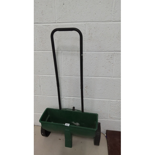 357 - Green plastic lawn and garden spreader with black metal handlebars and two wheels.