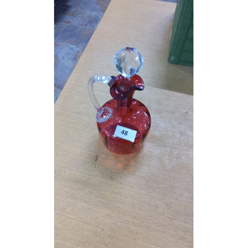 48 - Ruby red glass decanter with a clear faceted stopper and detailed handle.