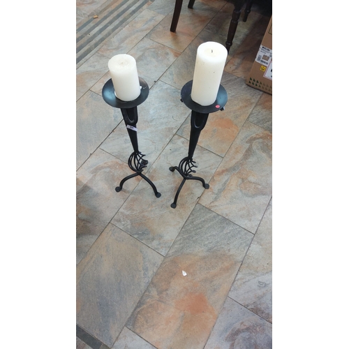 58 - Pair of black wrought iron candle holders with decorative bases, each holding a white pillar candle.... 