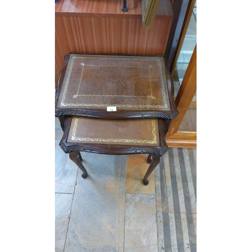 72 - Pair of nesting tables with wooden frames and leather inlaid tops, featuring intricate gold detailin... 